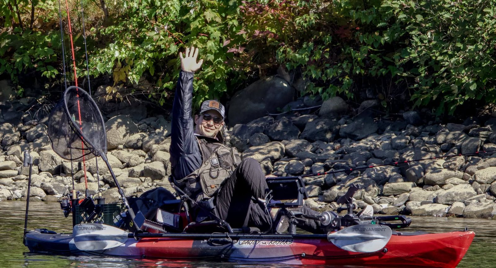 Matt DeSilva sitting in a rigged tournament fishing kayak on the water, raising a hand to the camera.